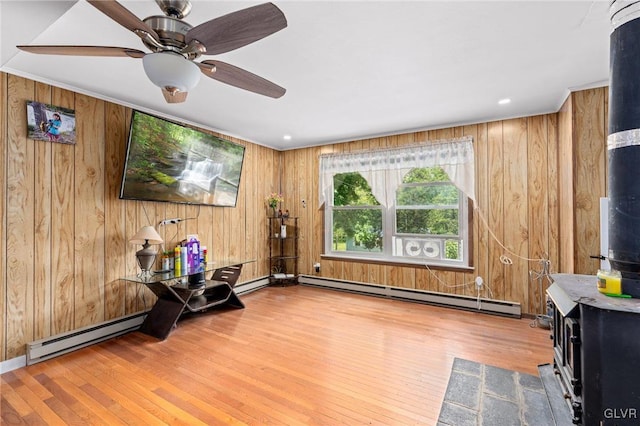 sitting room with wood-type flooring, wood walls, baseboard heating, and ceiling fan