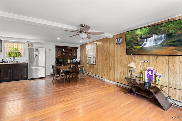 dining space with light hardwood / wood-style floors, wood walls, baseboard heating, and ceiling fan