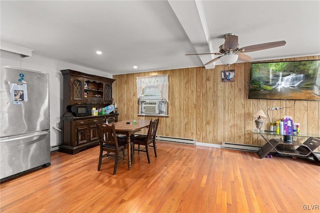 dining room with a baseboard heating unit, wooden walls, ceiling fan, and light hardwood / wood-style flooring