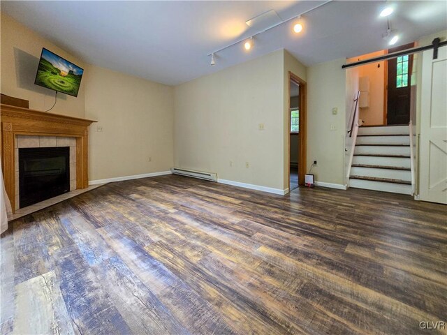 unfurnished living room featuring a tile fireplace, rail lighting, a baseboard radiator, a barn door, and dark hardwood / wood-style flooring