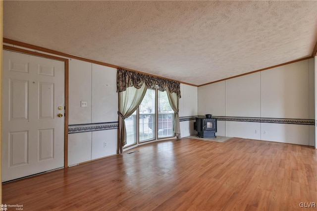 unfurnished living room featuring a textured ceiling, crown molding, light wood-type flooring, and a wood stove