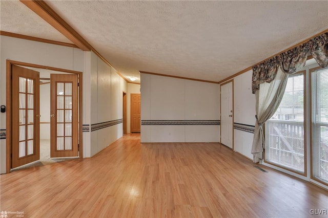 unfurnished living room featuring a textured ceiling, light hardwood / wood-style floors, ornamental molding, and french doors