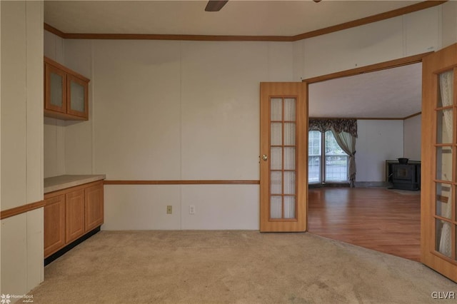 empty room featuring a wood stove, ceiling fan, light wood-type flooring, and crown molding