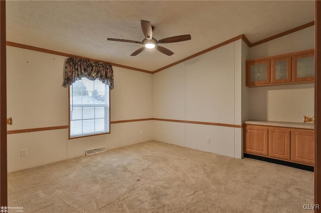 empty room with a textured ceiling, vaulted ceiling, light colored carpet, crown molding, and ceiling fan