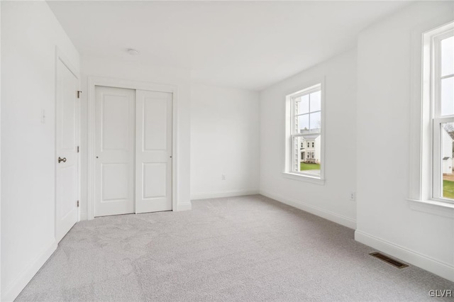 unfurnished bedroom featuring a closet, multiple windows, and light carpet