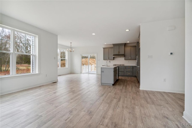 kitchen with an inviting chandelier, sink, an island with sink, light wood-type flooring, and decorative light fixtures