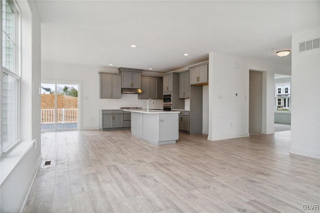 kitchen with light hardwood / wood-style floors, a center island with sink, cooktop, sink, and gray cabinets