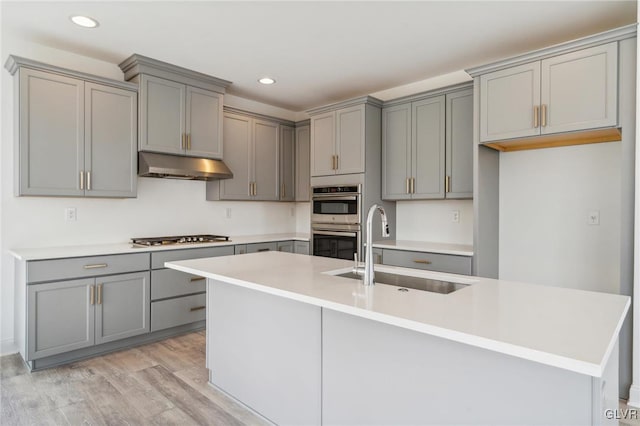 kitchen with light hardwood / wood-style floors, a center island with sink, sink, and gray cabinetry