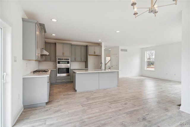 kitchen featuring an island with sink, gray cabinets, light hardwood / wood-style flooring, and appliances with stainless steel finishes