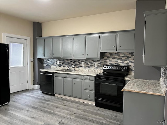 kitchen featuring gray cabinets, light hardwood / wood-style floors, tasteful backsplash, sink, and black appliances