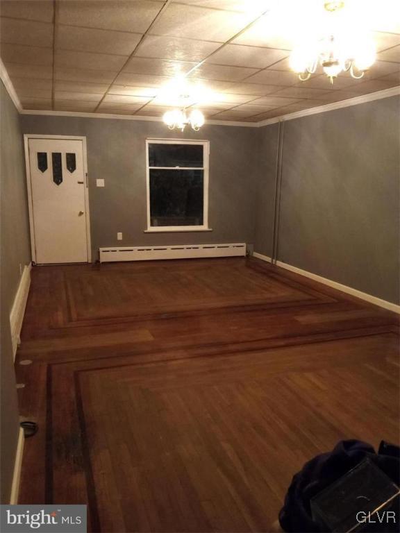 unfurnished room with a chandelier, baseboard heating, hardwood / wood-style floors, and crown molding