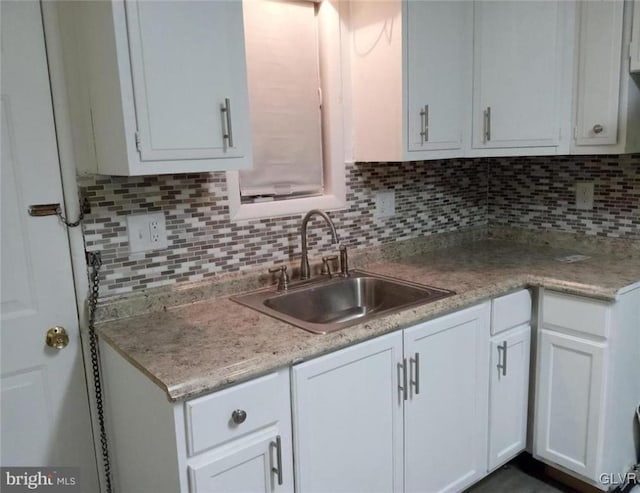 kitchen with backsplash, white cabinetry, and sink