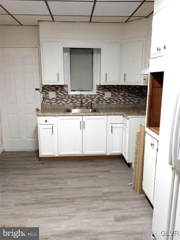 kitchen with a paneled ceiling, decorative backsplash, sink, and white cabinets