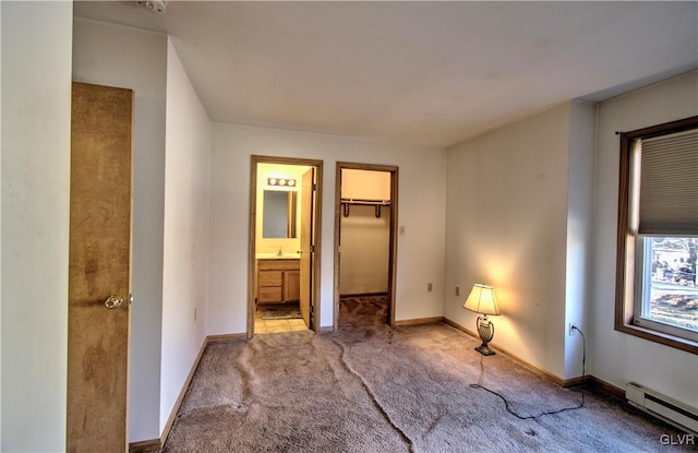 unfurnished bedroom featuring a walk in closet, a closet, baseboard heating, connected bathroom, and light colored carpet