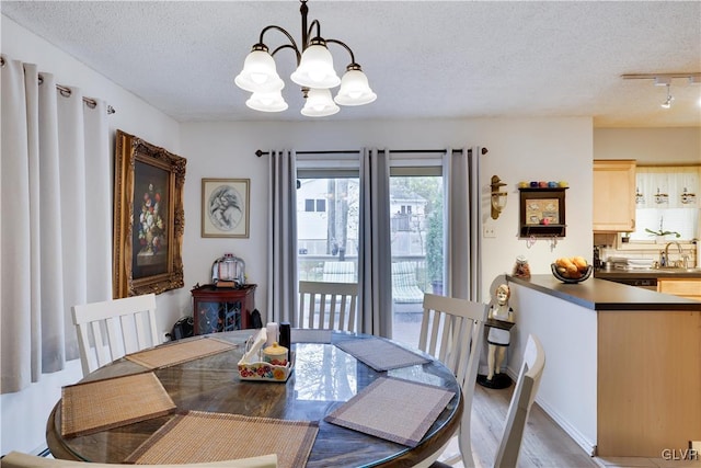 dining area featuring track lighting, a textured ceiling, light hardwood / wood-style floors, and a chandelier