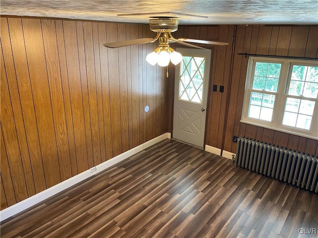 entrance foyer featuring a textured ceiling, wooden walls, dark hardwood / wood-style flooring, radiator heating unit, and ceiling fan