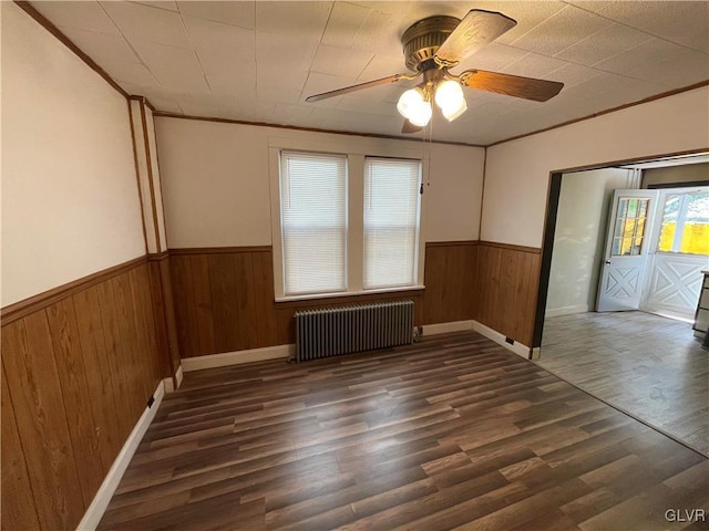 spare room with dark hardwood / wood-style flooring, radiator, wooden walls, crown molding, and ceiling fan