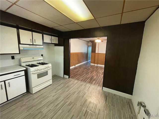 kitchen with light hardwood / wood-style floors, white cabinets, wood walls, a drop ceiling, and white gas stove