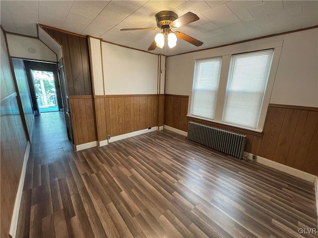 spare room with radiator heating unit, wooden walls, ceiling fan, and dark hardwood / wood-style floors