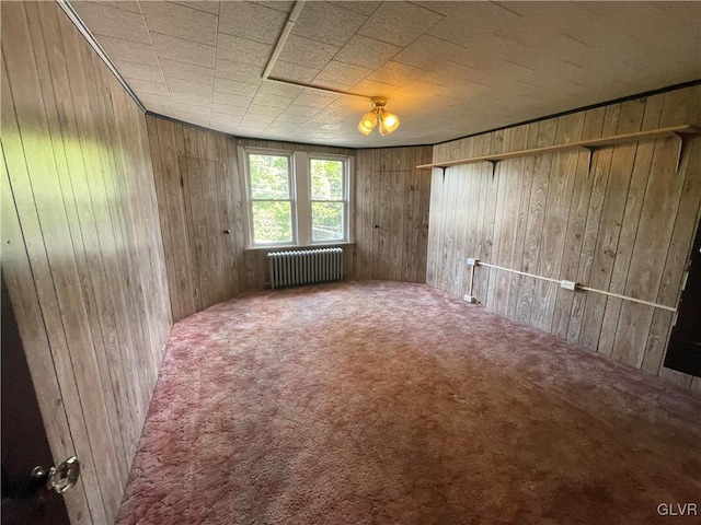 carpeted spare room with wood walls and radiator heating unit