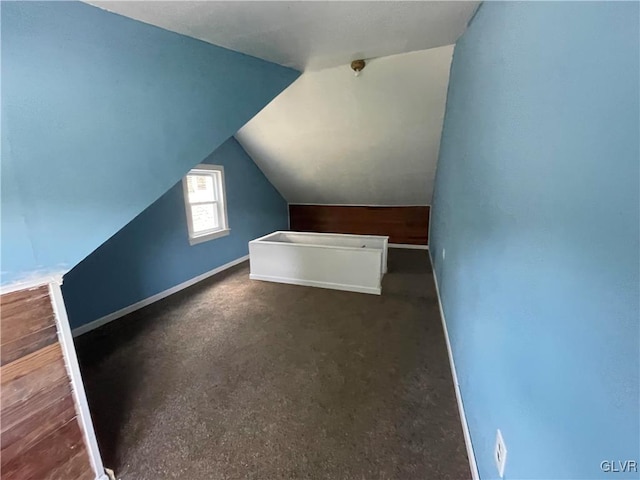 additional living space with dark colored carpet and vaulted ceiling