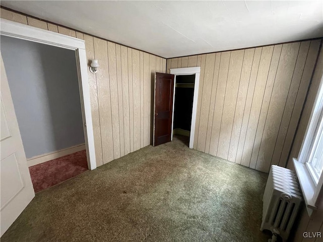 unfurnished bedroom with carpet flooring, wooden walls, and radiator heating unit