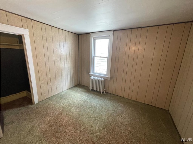 unfurnished bedroom with wood walls, carpet flooring, radiator, and a closet