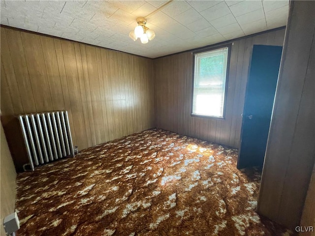 carpeted empty room with radiator heating unit and wooden walls