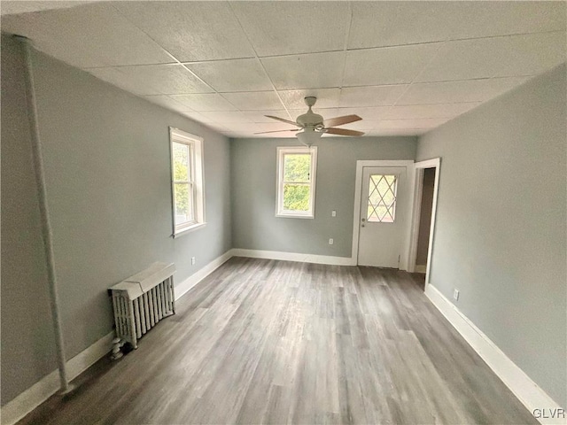 unfurnished living room with radiator heating unit, ceiling fan, hardwood / wood-style flooring, and a paneled ceiling