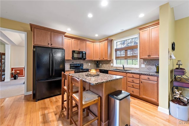 kitchen featuring dark stone counters, light wood-type flooring, black appliances, and sink