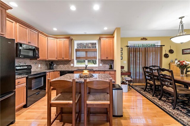 kitchen with decorative light fixtures, light wood-type flooring, stone countertops, and black appliances