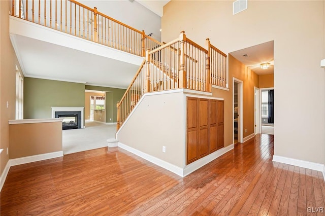 staircase featuring a towering ceiling, ornamental molding, and hardwood / wood-style floors