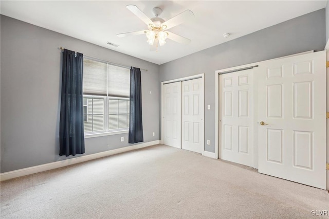 unfurnished bedroom with light carpet, ceiling fan, and two closets