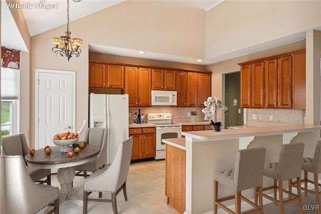 kitchen featuring kitchen peninsula, a notable chandelier, a kitchen breakfast bar, white appliances, and high vaulted ceiling