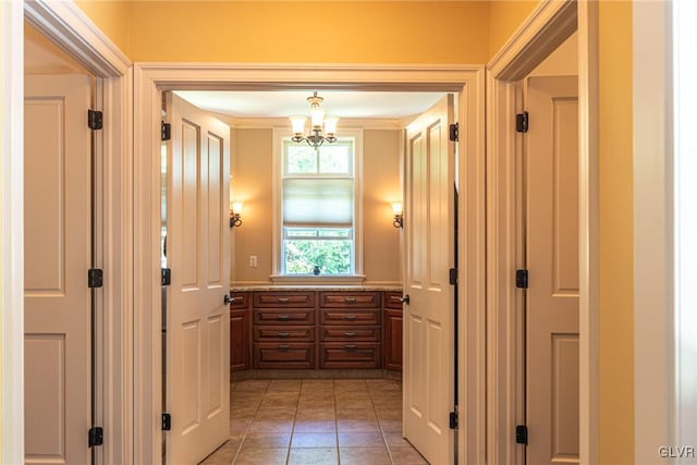 hallway with light tile patterned floors, a chandelier, and ornamental molding