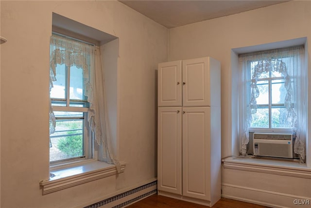 interior space with wood-type flooring, cooling unit, and a baseboard heating unit