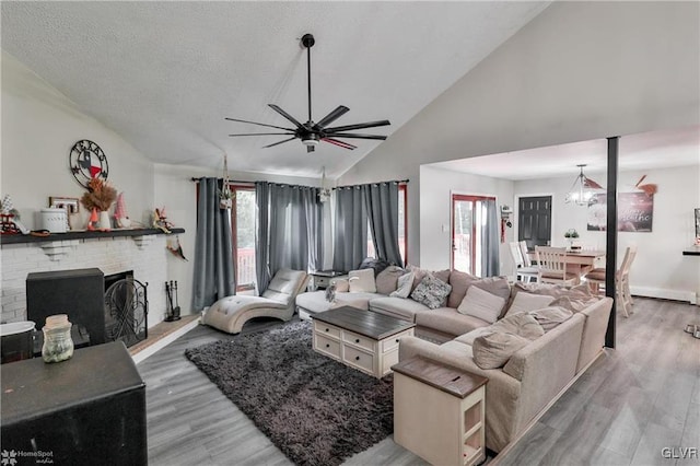 living room featuring wood-type flooring, a textured ceiling, high vaulted ceiling, a fireplace, and ceiling fan with notable chandelier