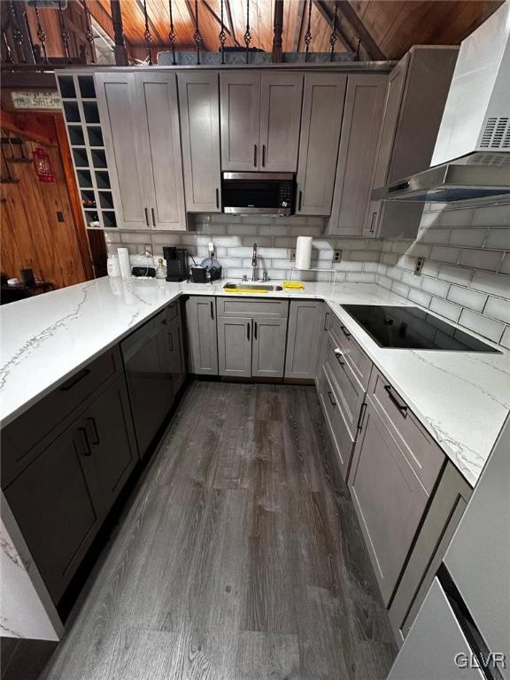 kitchen featuring sink, wall chimney exhaust hood, black electric cooktop, dark hardwood / wood-style flooring, and light stone counters