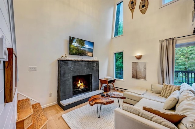 living room with a high ceiling, light hardwood / wood-style floors, a baseboard radiator, and a wealth of natural light