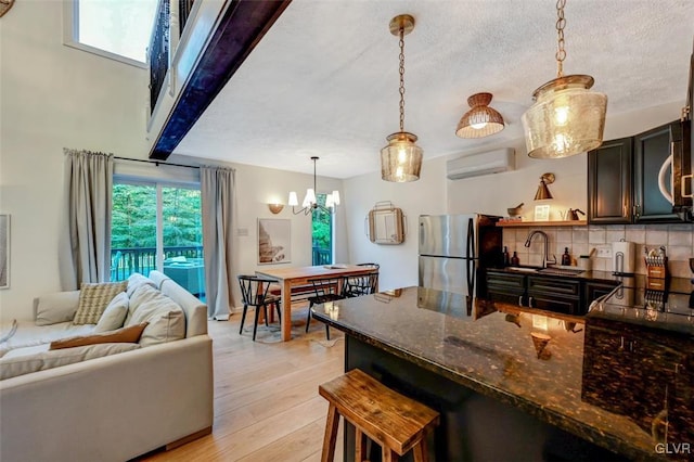 kitchen with hanging light fixtures, stainless steel refrigerator, an AC wall unit, light wood-type flooring, and dark stone counters