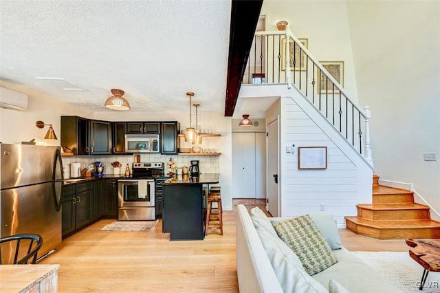 kitchen with appliances with stainless steel finishes, decorative backsplash, light wood-type flooring, decorative light fixtures, and a wall mounted AC