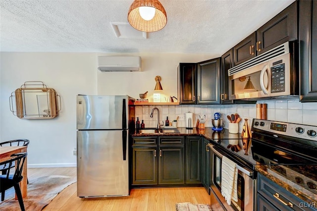 kitchen with tasteful backsplash, an AC wall unit, stainless steel appliances, light wood-type flooring, and sink