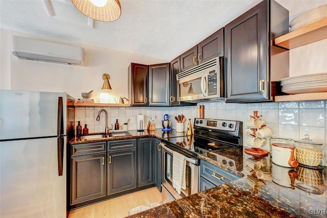 kitchen with a wall unit AC, appliances with stainless steel finishes, dark stone countertops, light wood-type flooring, and decorative backsplash