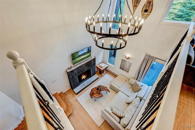 living room with a high ceiling, a chandelier, a premium fireplace, and hardwood / wood-style flooring