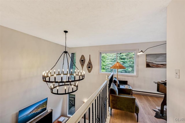 hall with an inviting chandelier, a baseboard heating unit, light hardwood / wood-style floors, and a textured ceiling