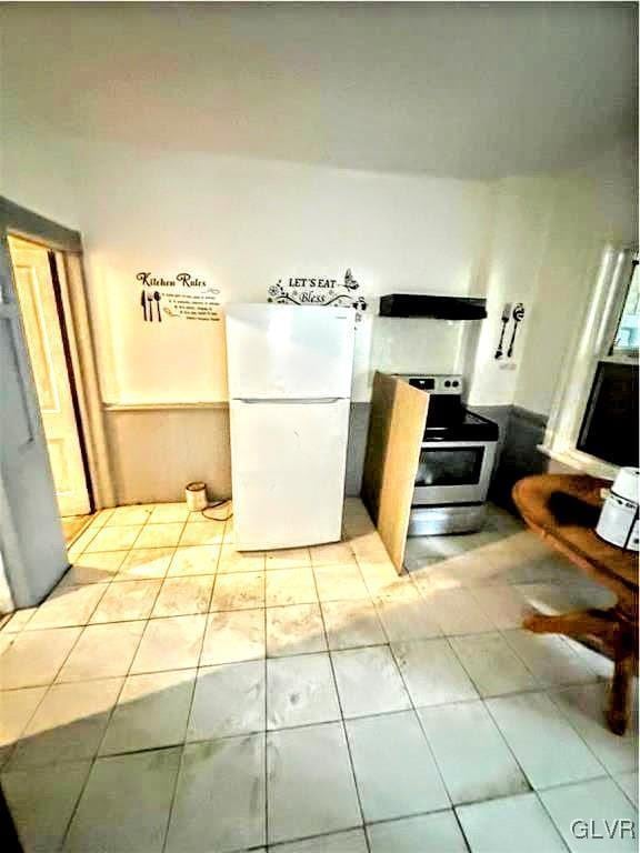 kitchen featuring light tile patterned flooring, range, white fridge, and ventilation hood