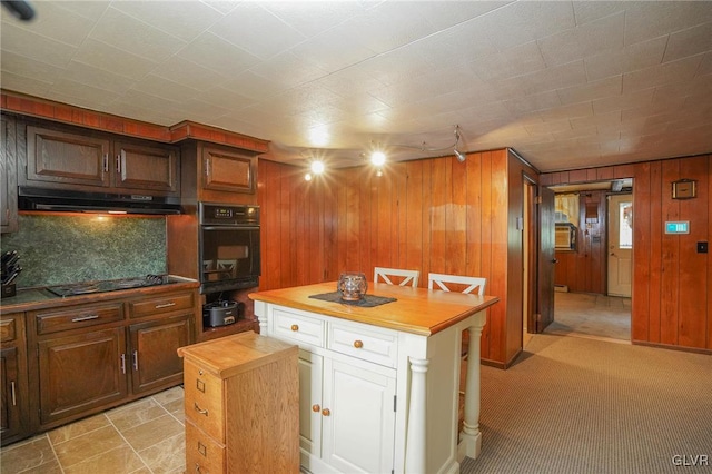 kitchen featuring tasteful backsplash, butcher block countertops, black appliances, a center island, and wooden walls