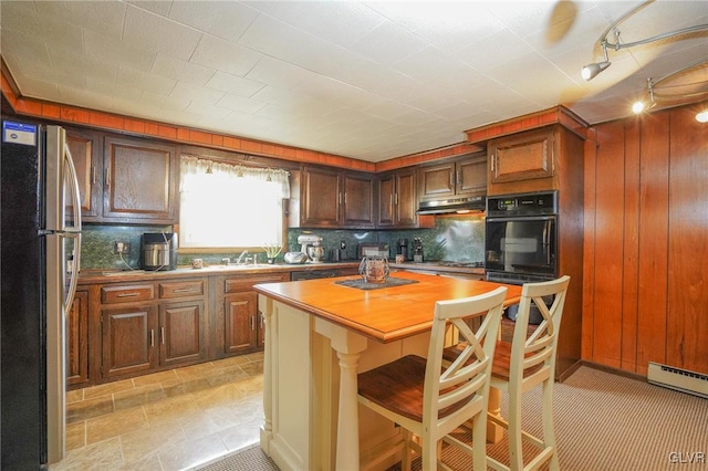 kitchen featuring stainless steel fridge, decorative backsplash, a breakfast bar, oven, and a baseboard heating unit