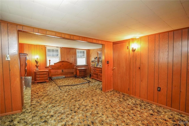 bedroom with wood walls, baseboard heating, and carpet flooring