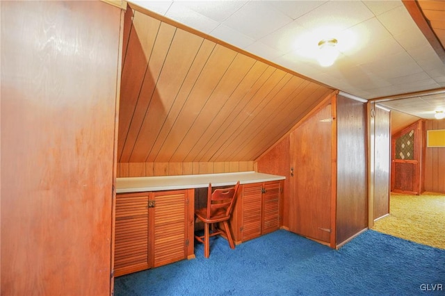 carpeted home office featuring wood walls and vaulted ceiling